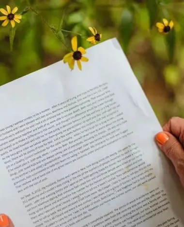 A person holding an open book with flowers in the background.