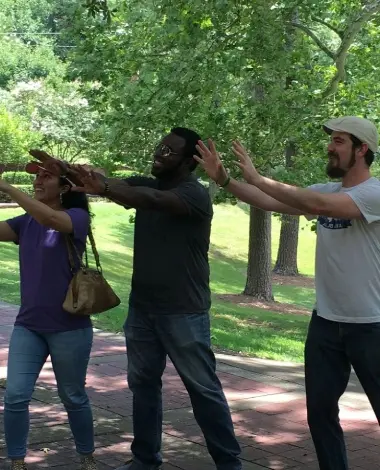 Three people are standing in a park and one is waving.