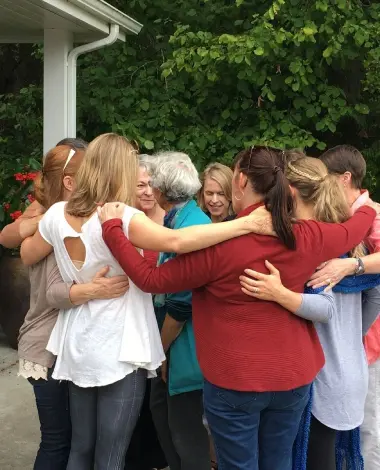 A group of women hugging each other in front of trees.
