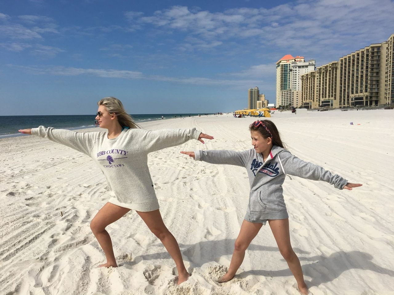 Two women are on the beach with their arms outstretched.