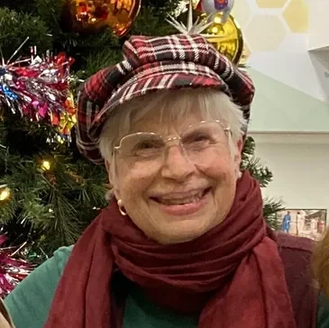 A woman wearing glasses and a hat near a christmas tree.